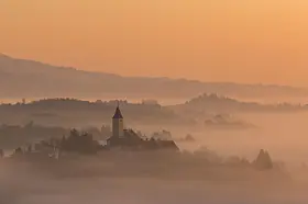 Church tower on a misty hill at sunrise with layered hills in the distance