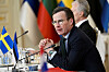 Ulf Kristersson speaks at a meeting beside Swedish flags and microphones.
