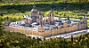 Aerial view of a vast, ornate monastery with domed towers, surrounded by dense forest in a mountainous landscape.