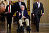 Mitch McConnell sits in a wheelchair as aides escort him through a Capitol corridor.