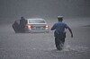 Police officer wading through heavy rain and floodwater towards a stranded car.
